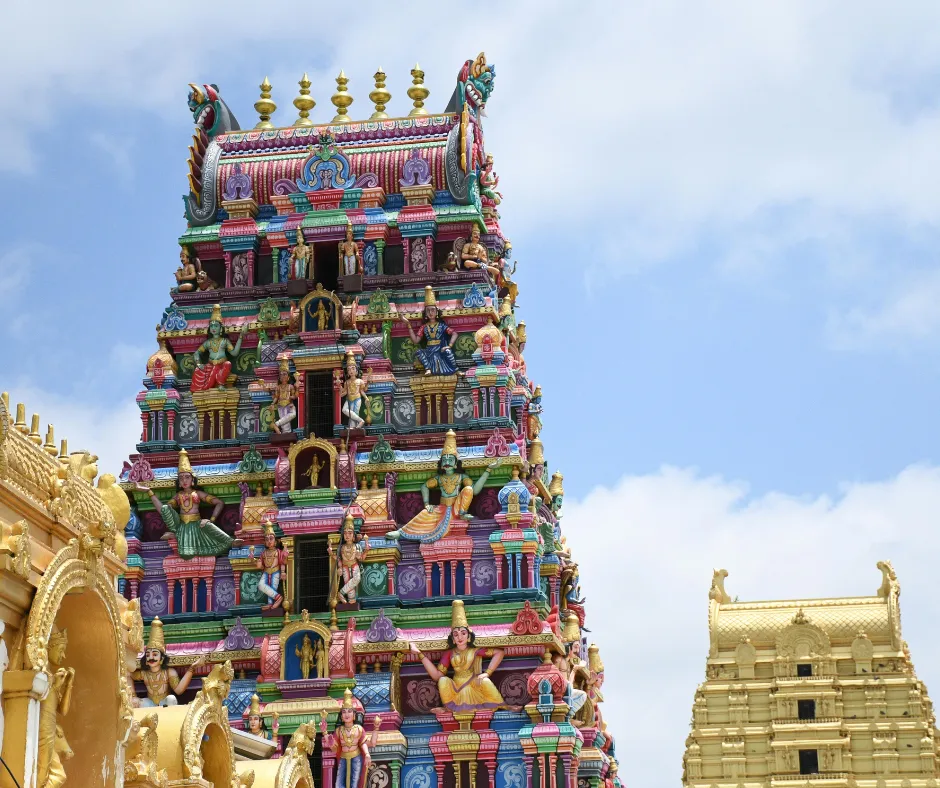 Colorful Hindu temple tower with intricate deity carvings against a clear blue sky.