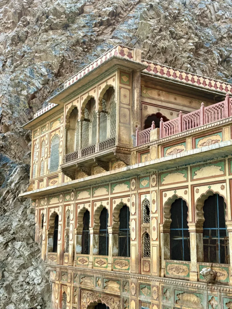 Historic ornate building with arches against rugged rock face, ancient architecture.