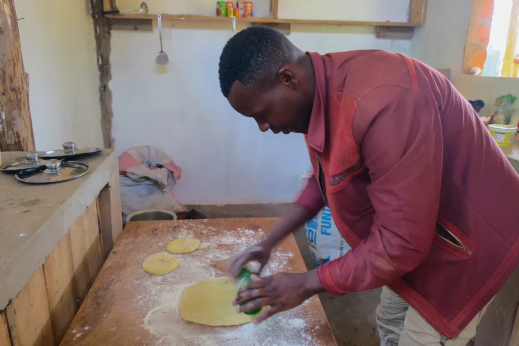 Man in red jacket rolling dough on flour-dusted wooden table in rustic kitchen.