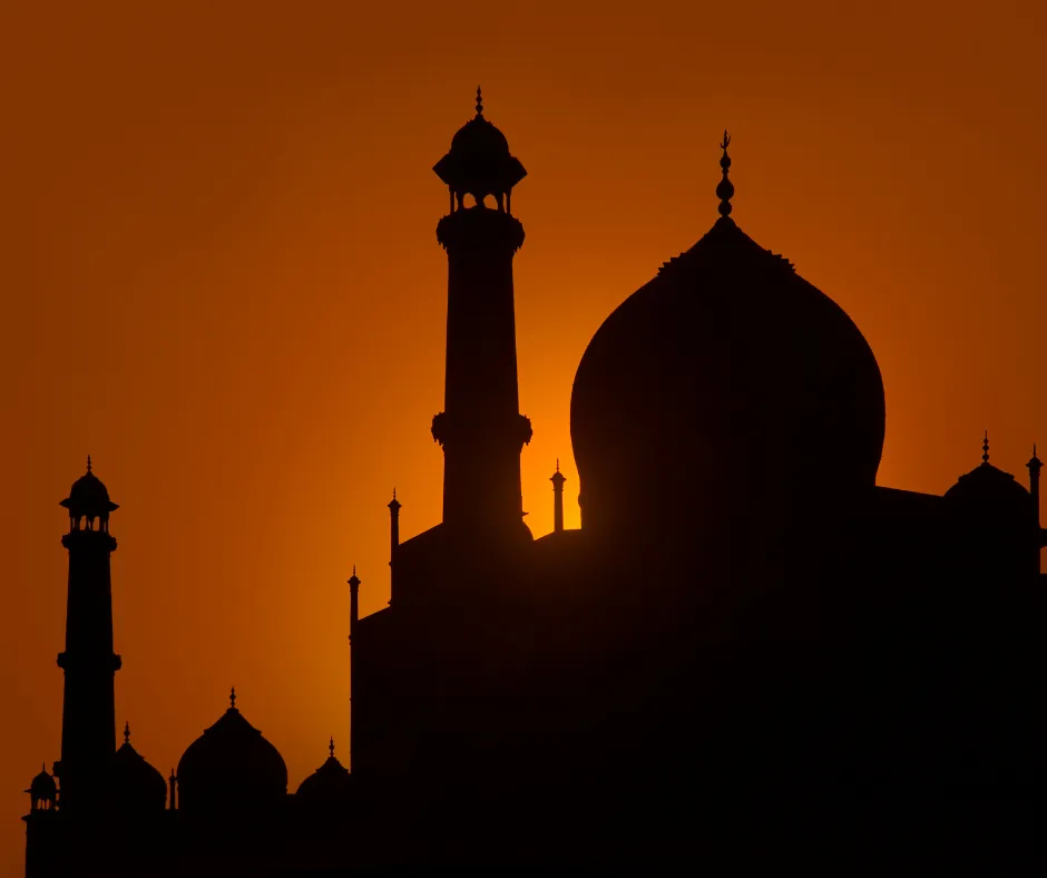 Silhouette of domed mosque with minarets at vibrant orange sunset