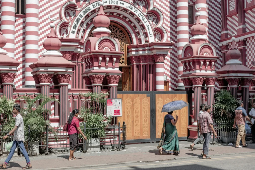 People walking past vibrant red-white patterned building with arches and urban charm.