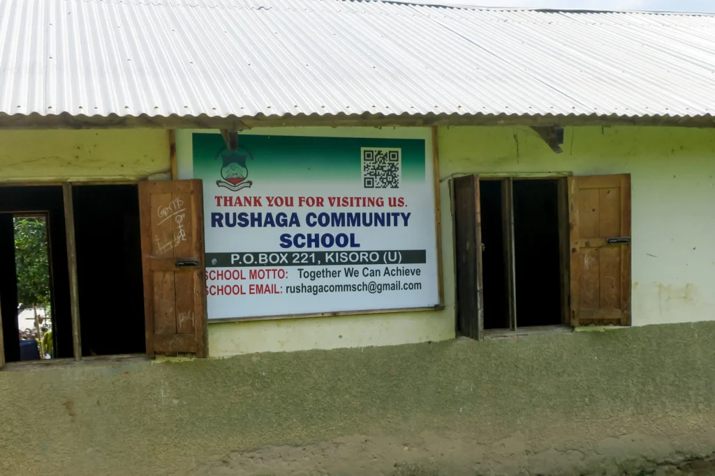 Rushaga Community School exterior with sign, motto, contact, and open window.