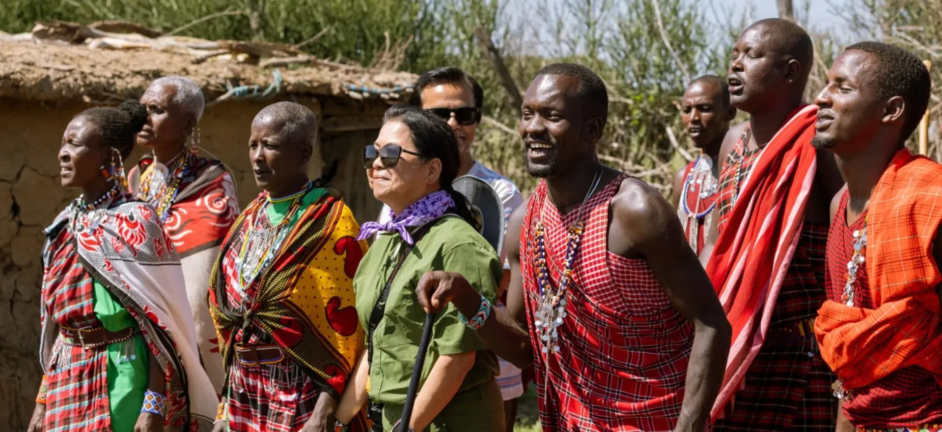 Maasai villagers and tourist smiling outside traditional mud house during cultural experience.