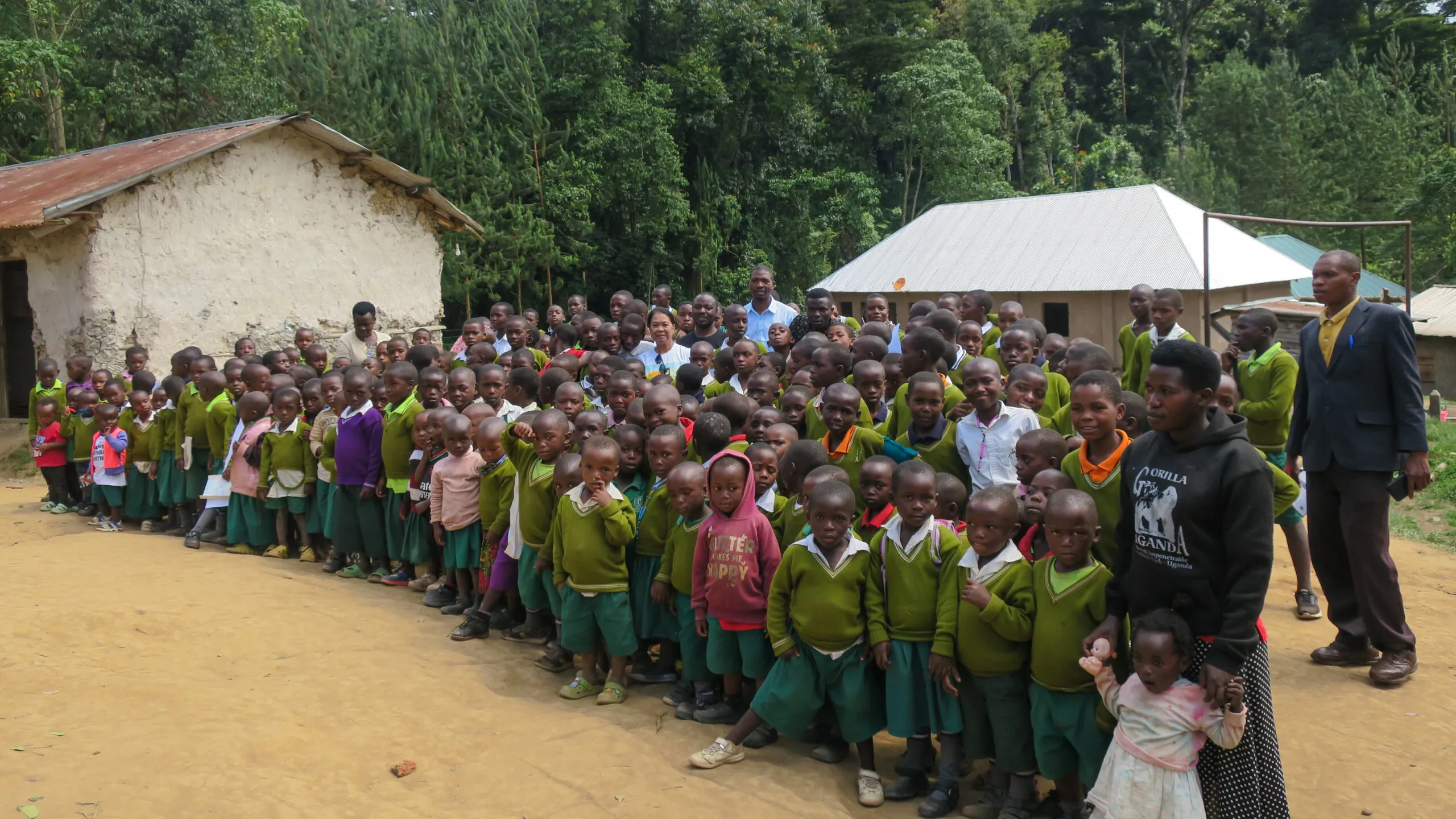 Joyful children in green school uniforms posing outdoors with adults and trees.