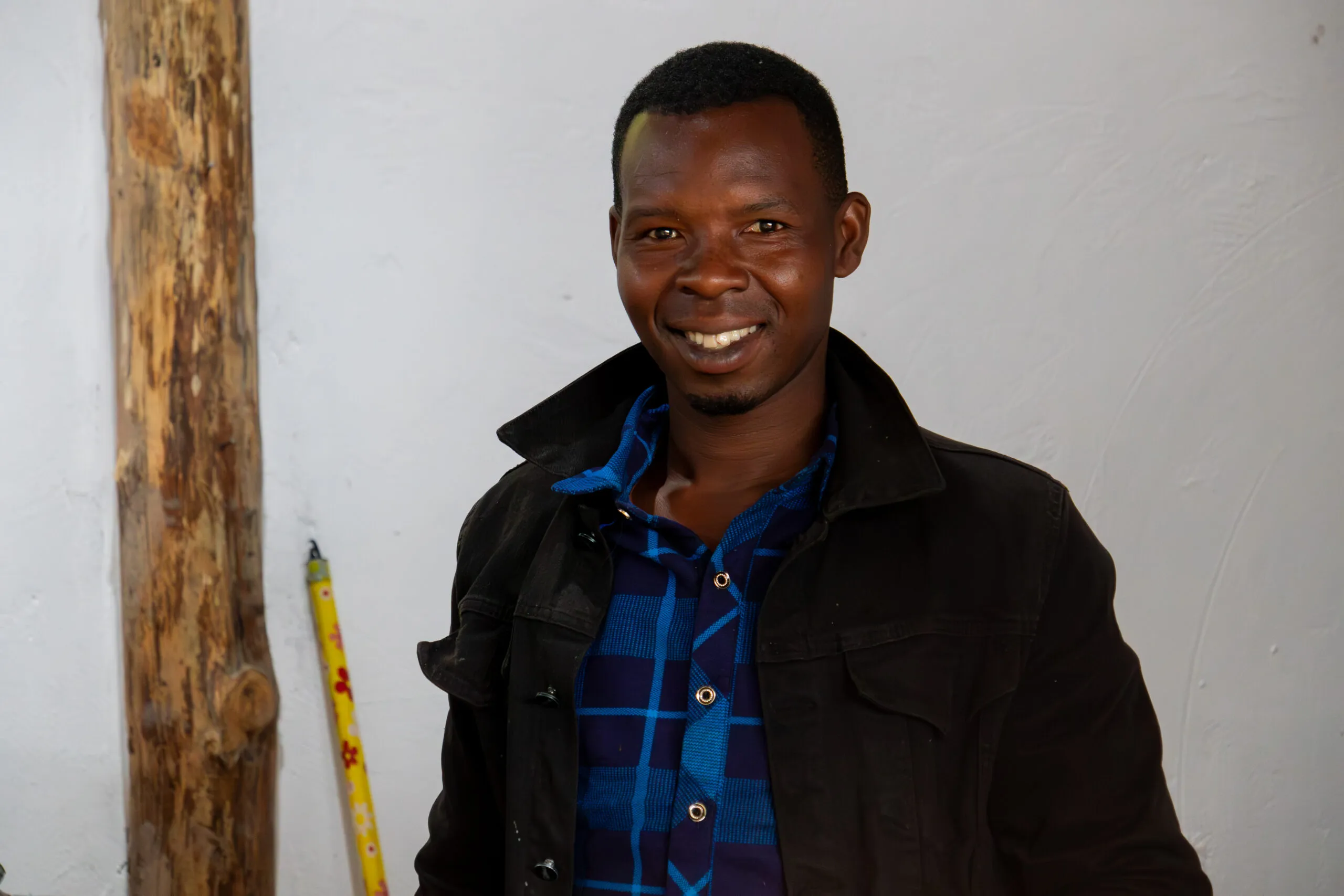 Smiling man in black jacket and plaid shirt indoors with measuring tools.