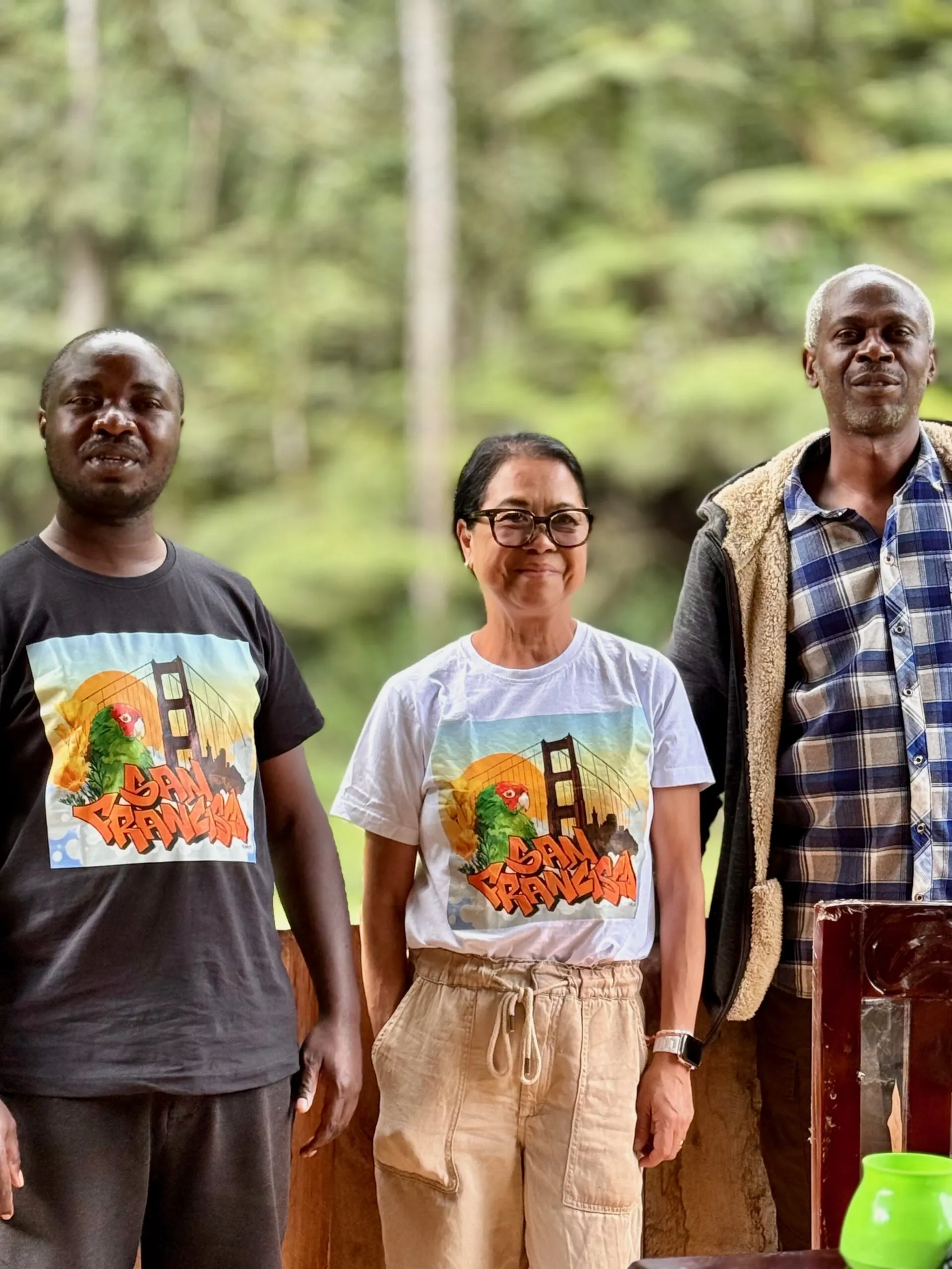 Three smiling people outdoors wearing San Francisco shirts amid lush green nature.