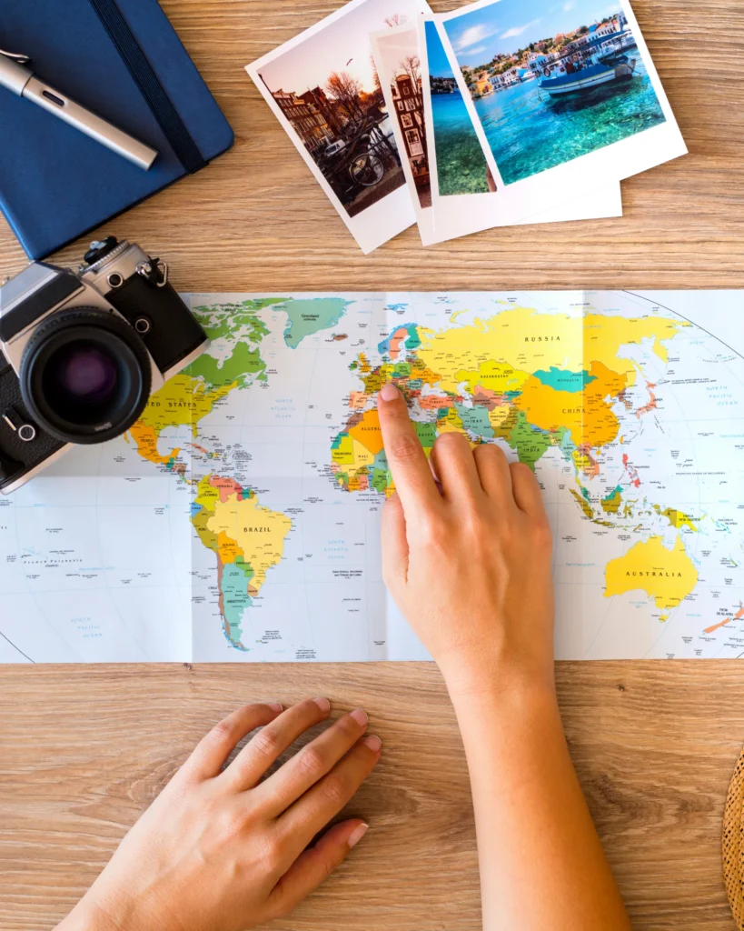 Hands pointing at map with camera, notebook, pen, photos, planning travel adventure.