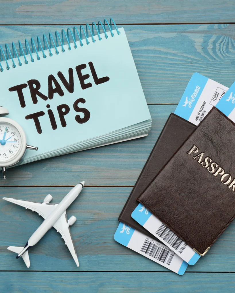 Travel essentials flat lay: notebook, passports, boarding passes, clock, airplane on blue.