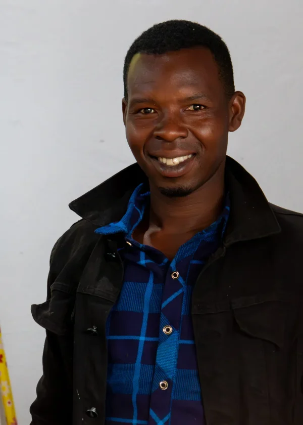 Smiling man in black jacket and plaid shirt indoors with measuring tools.