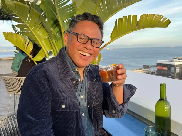 Smiling man with drink on rooftop ocean view, sunny relaxed vibe.