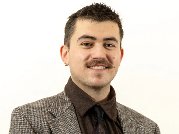 Smiling professional man in brown shirt, patterned tie, tweed jacket.